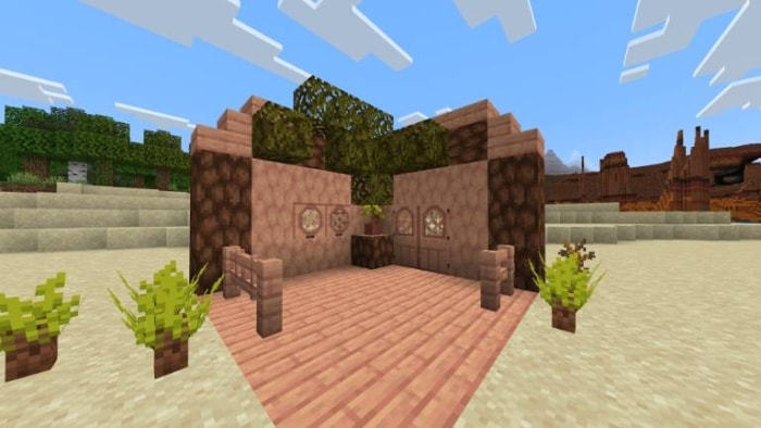 Wooden hut with plants on sandy terrain.