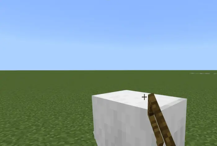 Hand holding tool near white block on grass.