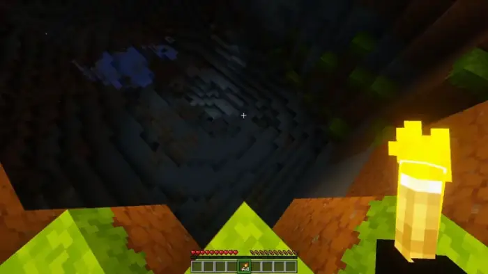 Player holding glowing torch above a dark cave