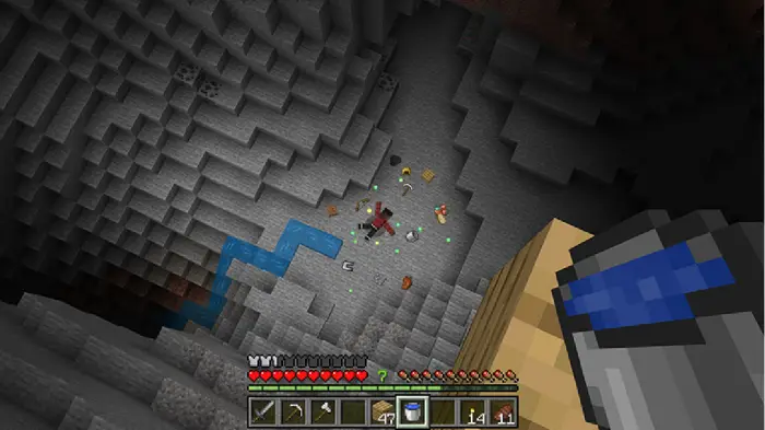 Player looks down a deep cave with dropped items.