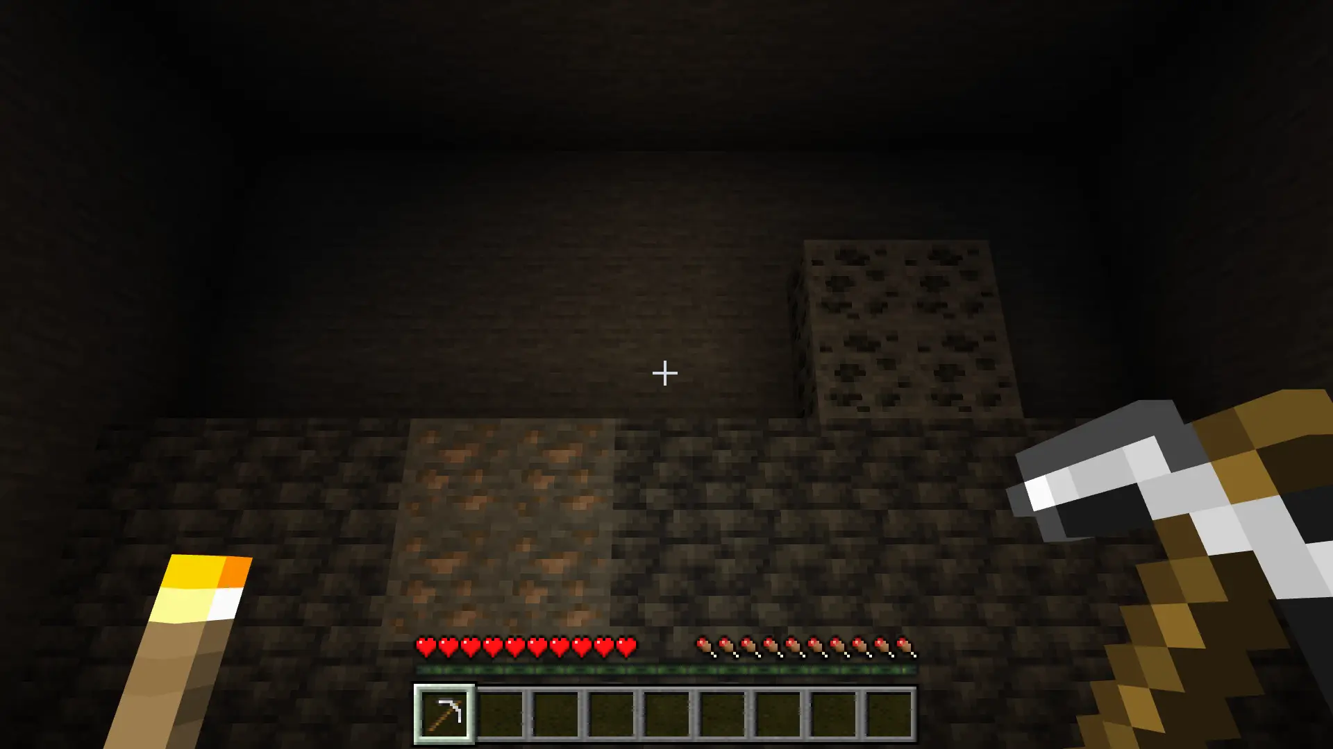 A torch lights a cave from the offhand while the player holds a pickaxe